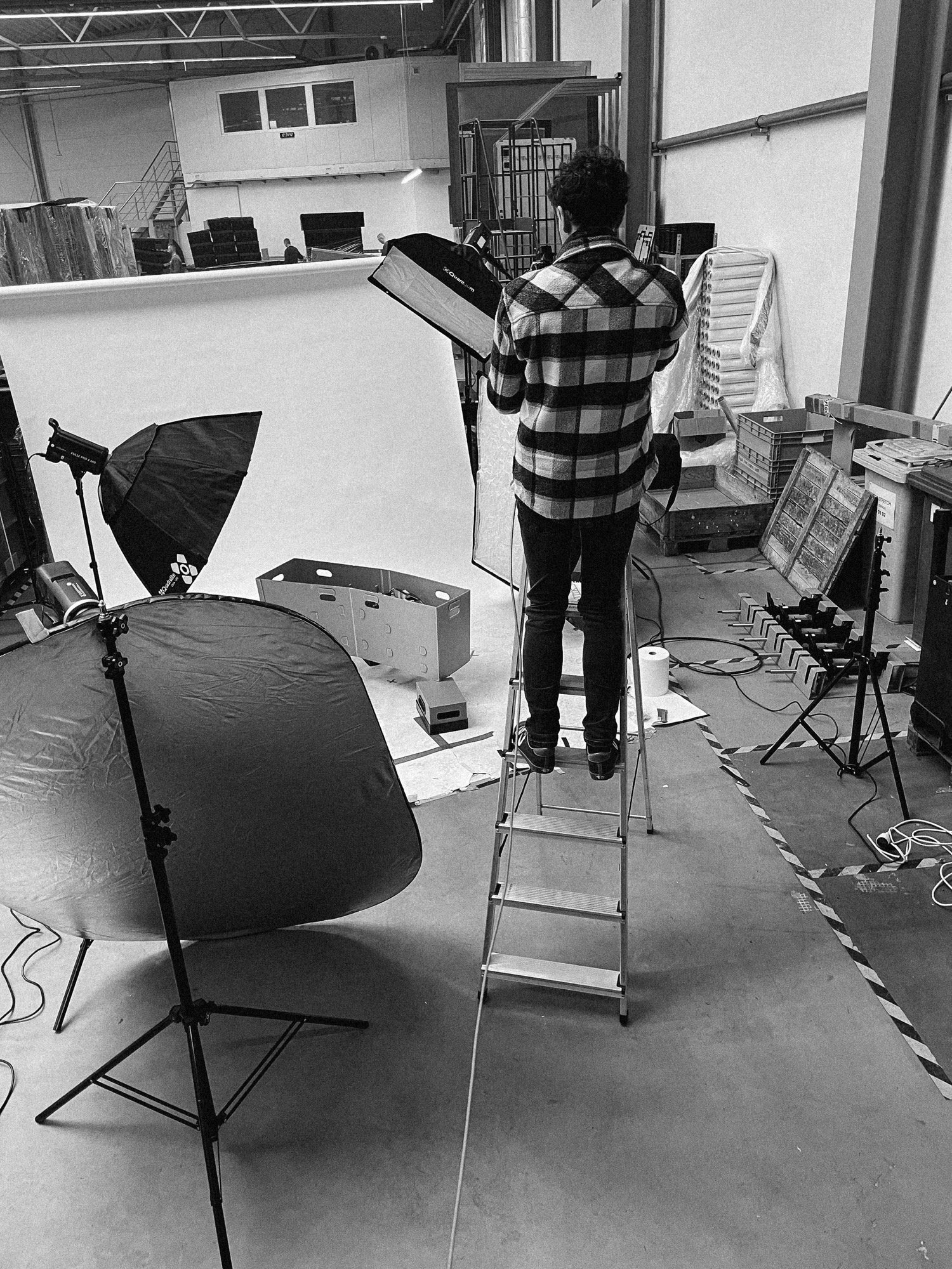 Softbox na drabinie — budowa oświetlenia packshotu na hali magazynowej, kadr B&amp;W