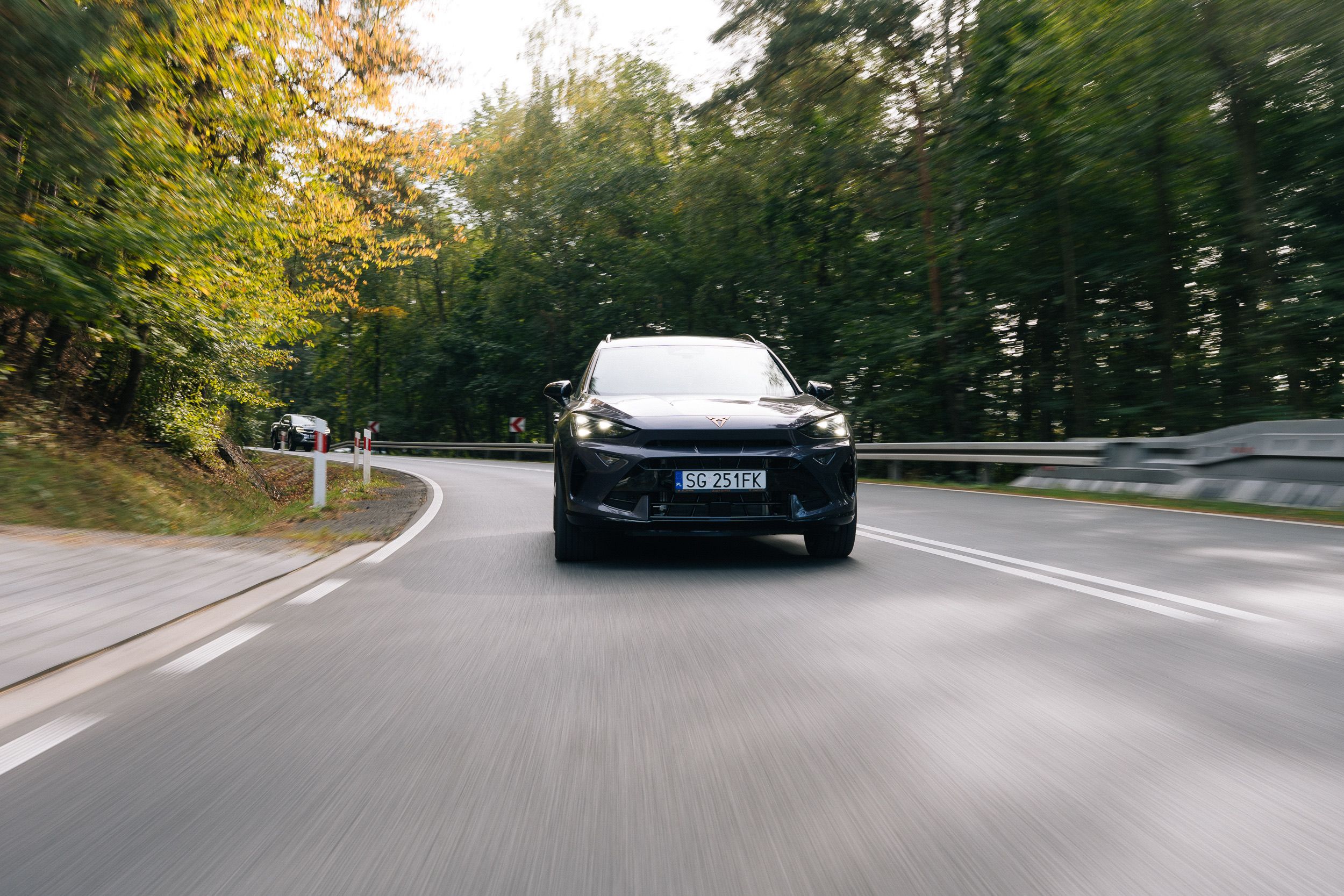 Ein dunkler CUPRA SUV kommt in einer Kurve einer Waldstraße frontal entgegen