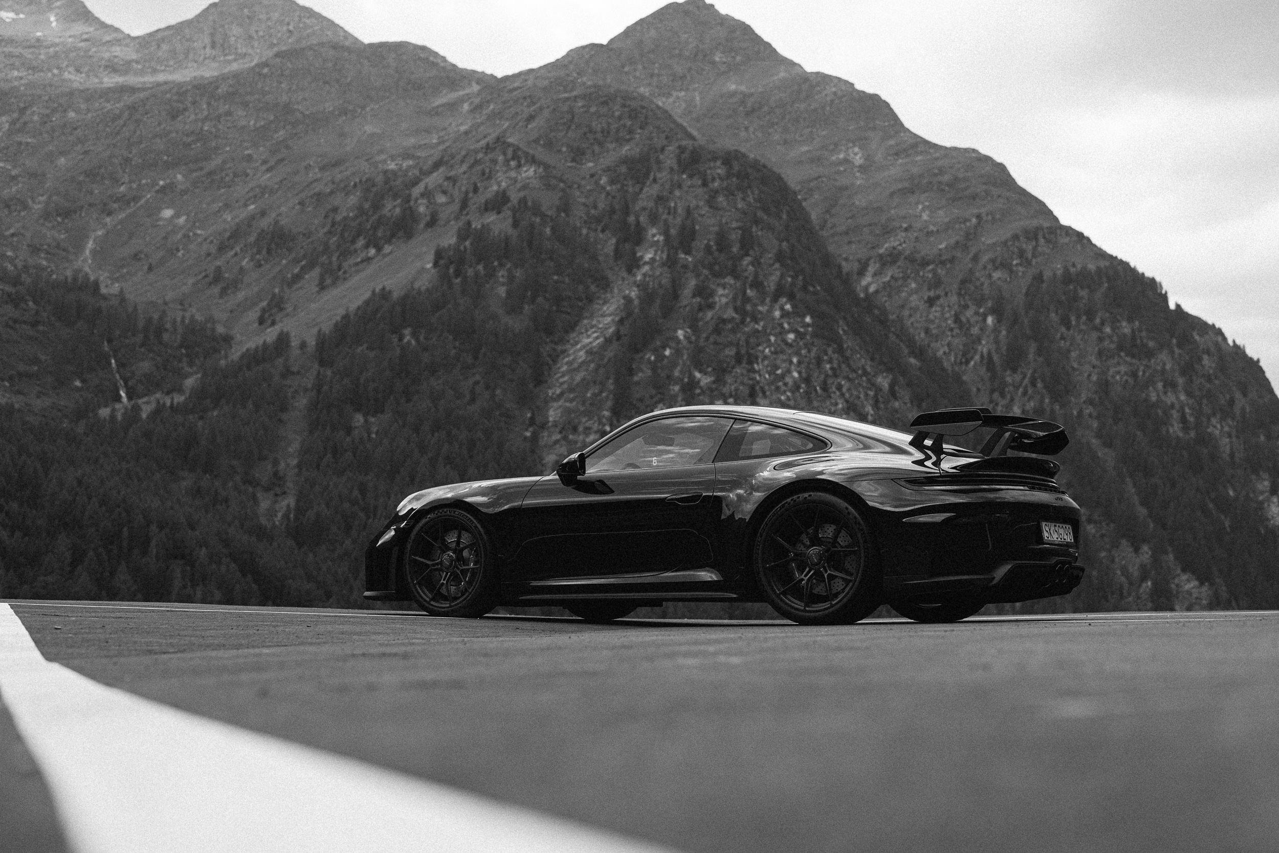 911 GT3 z profilu, z niska, na pustym placu pod zalesionymi szczytami — kadr czarno-biały