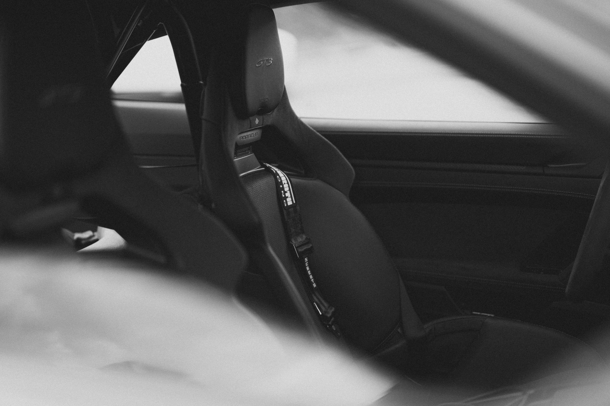 Pusty fotel kubełkowy z pasami widziany przez szybę 911 GT3 — kadr czarno-biały